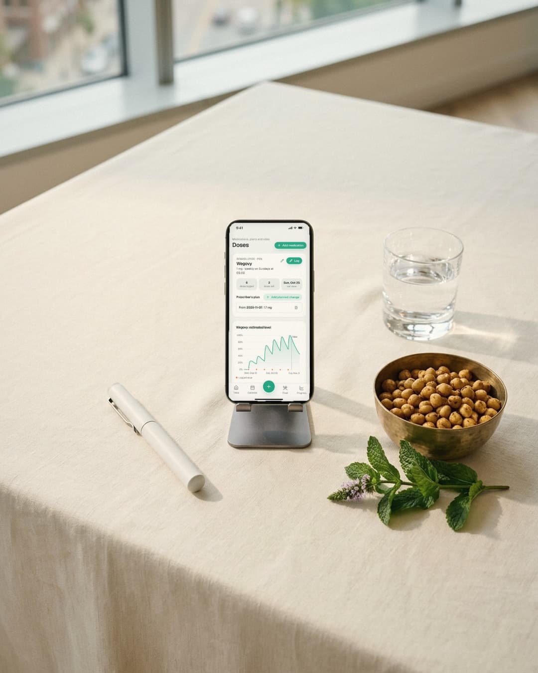 A phone on a stand shows the Doses screen next to a plain injection pen, a glass of water and roasted chana.